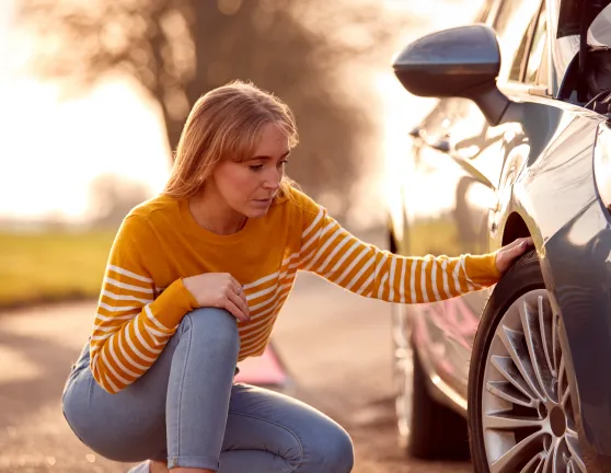 Persona preocupada mirando el neumático de un coche
