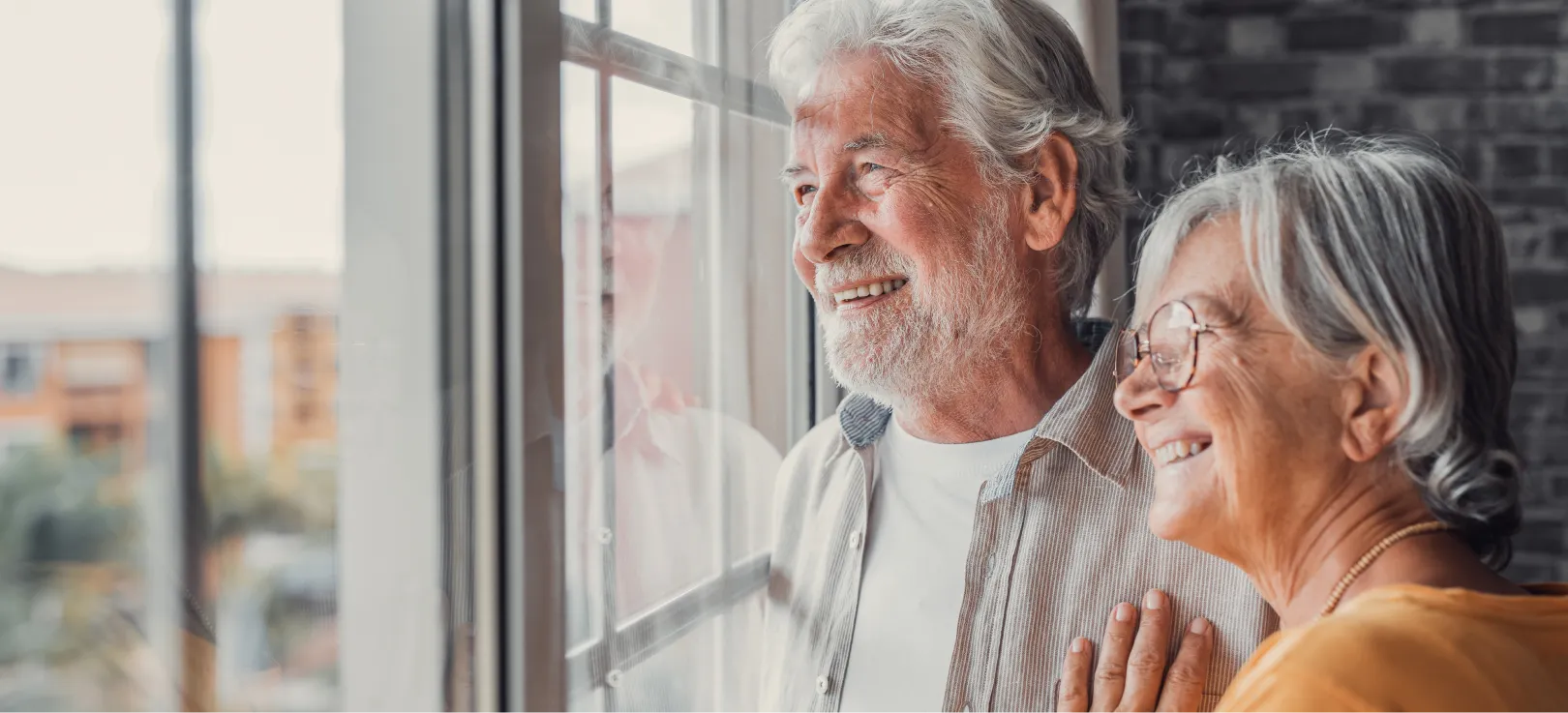 Pareja de ancianos mirando por la ventana de su casa mientras sonríen